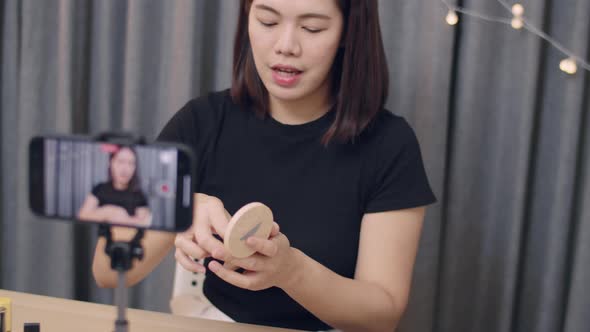 Young Asian woman beauty blogger influencer makeup artist recording on smartphone.