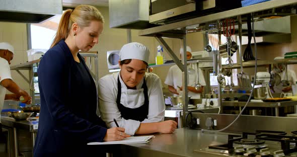 Female manager and female chefs discussing over clipboard 4k alt