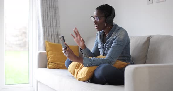 Woman sitting on sofa having video call on smart phone with headphones