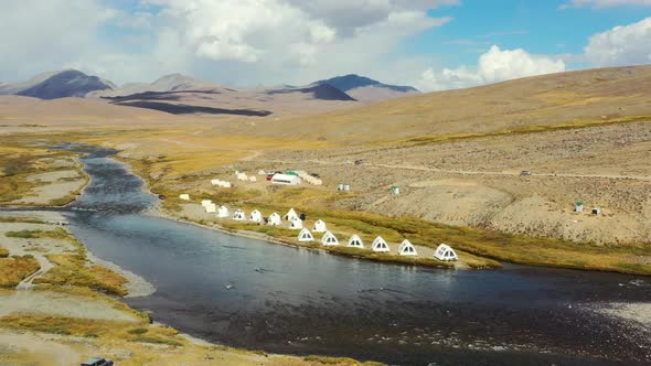 Aerial drone panning across a natural river with white luxury glamping tents in the high-altitude al alt