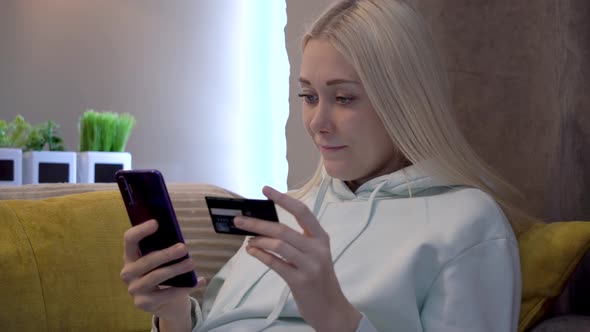Young female customer using mobile phone while sitting on sofa at home. alt