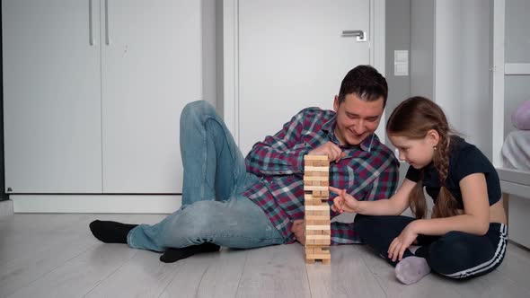 Father and daughter. They play tower and laugh. They sometimes look at the camera. Positive emotions alt