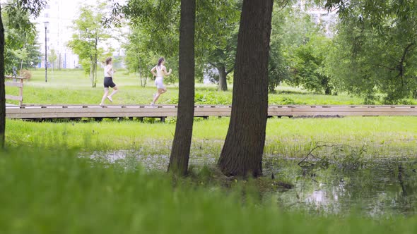 Women with Ponytails Run Along Wooden Track in Public Garden