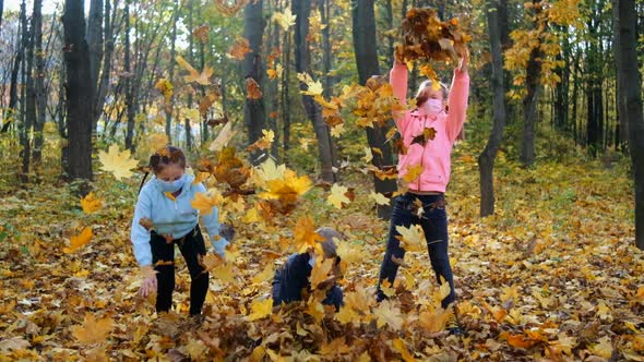 Small children in medical masks throw fallen yellow leaves in the Park on an autumn day. 