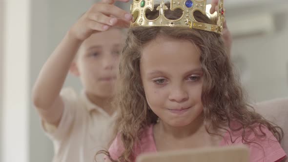 Cute Boy Putting the Crown on the Head of Adorable Curly Girl Looking in the Mirror. Gallant Boy alt