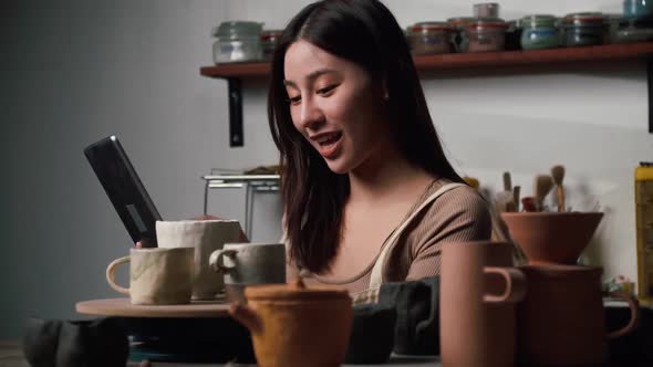 A young female ceramicist is busy checking orders for ceramics for a customer. alt
