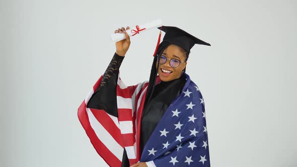 Happy Stylish Afro American Woman Student In Graduate Uniform Shows Diploma Holding USA Flag On alt