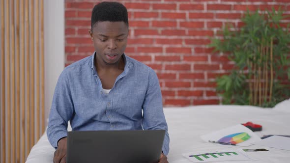 Young African American Man Sighing and Falling Back on Bed in Home Office alt