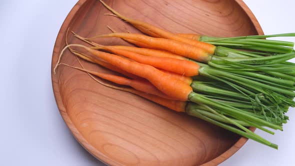 Young Carrots Rotation in a Wooden Bowl on a White Background Top View