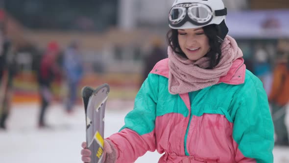 Portrait of Happy Female Skier with Skis Standing Outdoors Exhaling and Looking Around alt