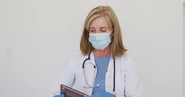 Portrait of caucasian senior female doctor wearing surgical gloves and face mask using tablet comput alt