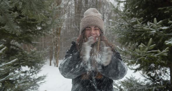 Playful Young Woman Throws Snow Up and Smiling in Front of the Tree in Forest