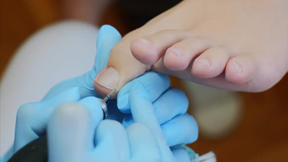 Pedicurist Master in Blue Gloves Makes Hardware Pedicure in Beauty Salon