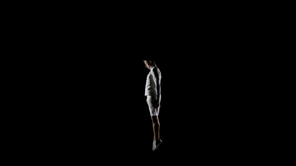 Handsome Male Gymnast in White Clothes on a Black Background Jumping on a Trampoline in Slow Motion alt