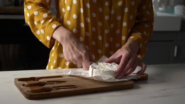 Female in yellow polka dot shirt with a cheese on table in kitchen