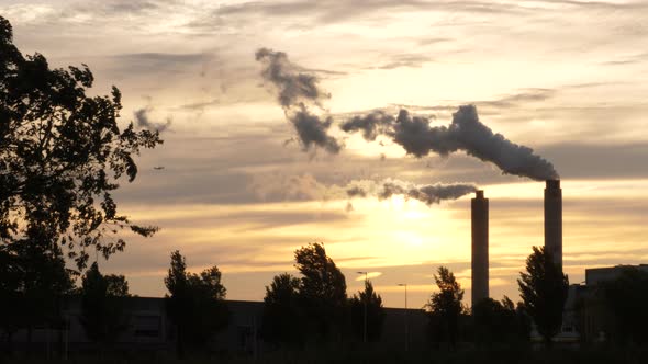 Smoke rises from an industrial smokestack at sunset