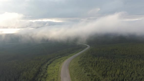Beautiful View of Scenic Road From Above Surrounded By Lush Forest, Clouds and Mountains alt