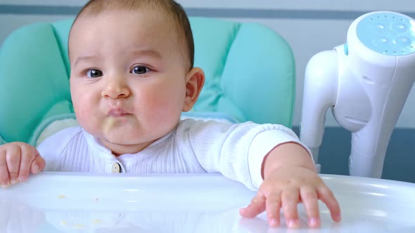 A hungry baby taps his hand on the table on a high chair, asks to eat, nibbles on a spoon. Teething, alt