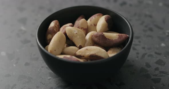 Slow Motion Man Hand Takes Brazil Nuts From Black Bowl on Terrazzo Countertop alt