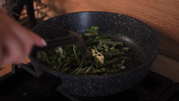 Woman Stir Fried Green Beans in a Frying Pan with a Plastic Black Spoon