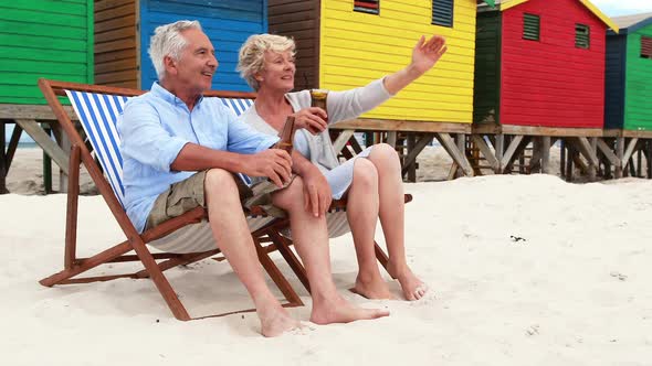 Senior couple toasting drinks near colorful beach hut alt