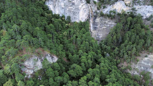 Aerial footage of a waterfall in rocky green forests high at the mountains