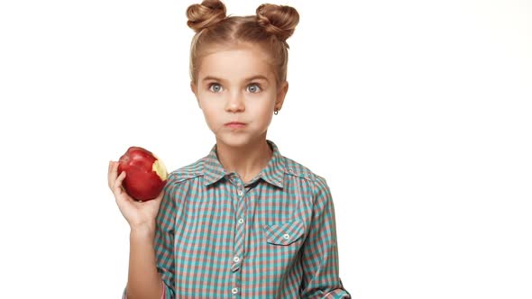 Small Cute Caucasian Caucasian Kid Girl with Plaid Shirt and Two Hair Buns Eating Red Apple with alt