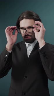 Handsome Young Guy with Long Hair in a Black Suit and Shirt Taking Off the Glasses alt