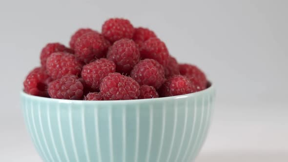 Ripe Raspberries in a Bowl Rotates on a Light Background
