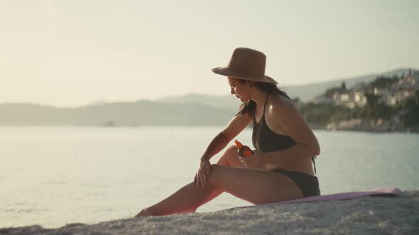 Girl Applies Sun Protection Cream on the Body on the Beach Near the Ocean alt