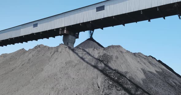 Black Coal Pile on Mine Coal Pours Down in Huge Black Pile From Covered Conveyor Belt at Blue Sky alt