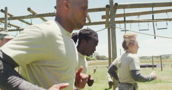 Diverse fit group in army fatigues running in the sun at army obstacle course in field alt