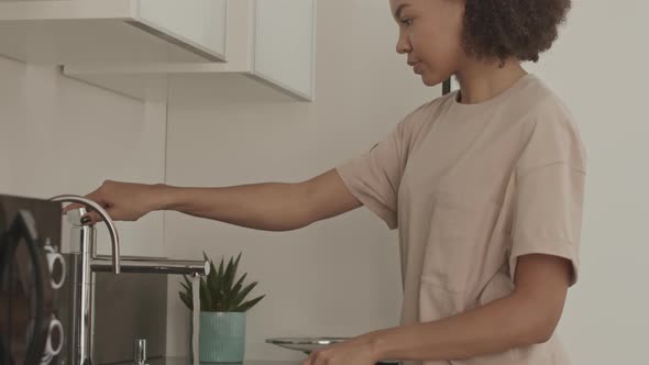 Young Woman Washing Dishes in Apartment alt