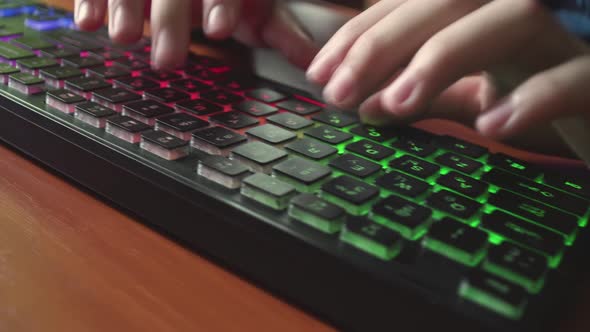 A Man Types Text on a Backlit Keyboard alt