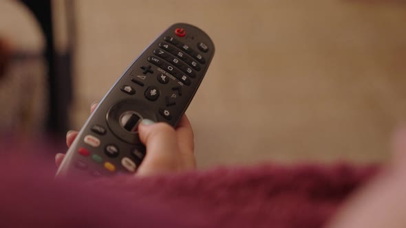 Close up of woman hand holding television remote scrolling through menu on couch alt