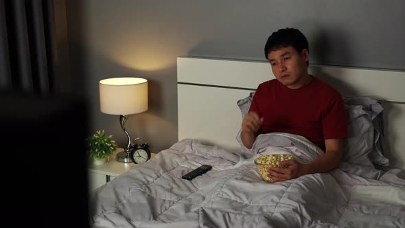 sad young man watching television and crying on a bed at night (romantic movie)
