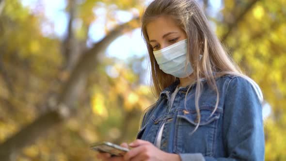 Portrait Woman in Protective Medical Mask Walks Down To the Street Uses Phone Texts Scrolls Surfs alt