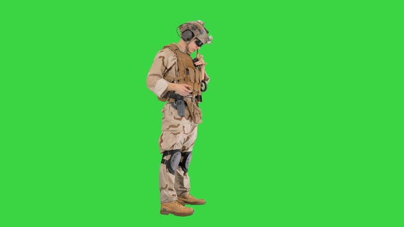 Soldier Standing and Talking on the Radio on a Green Screen, Chroma Key. alt