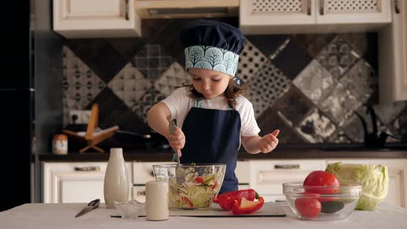 Little Girl Plays in Kitchen As a Cook, She Mixes Chopped Vegetables in a Plate alt