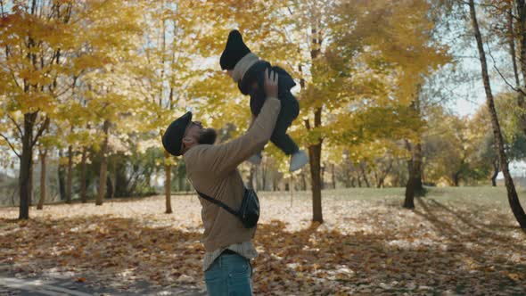 Father Raises His Son to the Sky in the Yellow Autumn Park on a Sunny Day alt