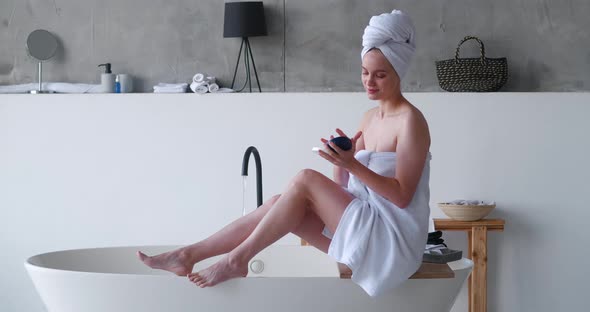 Halfnaked Beautiful Woman Wrapped in White Bath Towels Applies Moisturizer to Her Legs Makes a alt