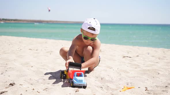 Happy Boy Playing with Cars on a Sandy Beach Against a Beautiful Sea and Blue Sky