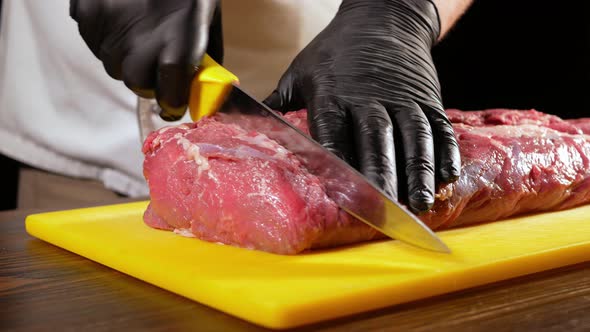 A Professional Butcher in Black Gloves Slices a Piece of Raw Meat for Steak From Entrecote