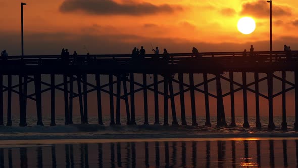 People walking across pier during colorful sunset alt