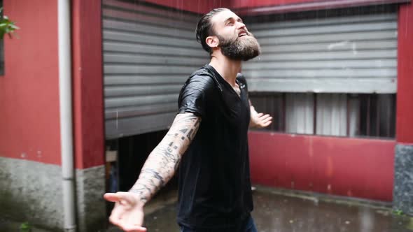 Young bearded tattooed man feeling free under the pouring rain alt
