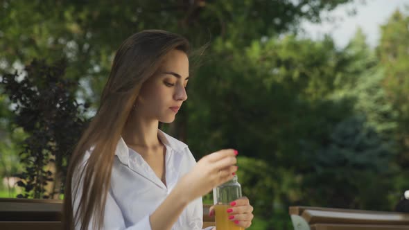 Young Beautiful Woman Drinking Orange Juice Outdoors at Summer Park alt