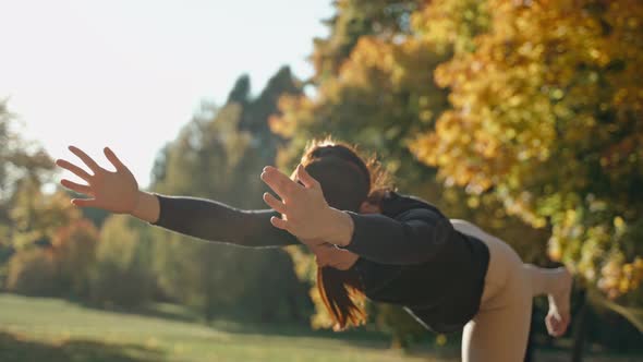 Young Woman Practices Warrior Yoga Pose in Sunny Autumn City Park on a Mat