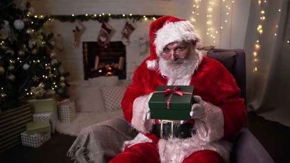 Funny Santa Claus Holds Out a Box Of Christmas Gifts To the Camera. Choosing New Year's Gifts. Santa