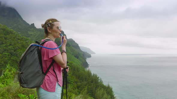 Woman Drinking Water During Hike By Kalalau Trail with Cinematic NaPali Coast alt