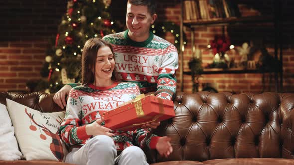 Happy Surprised Woman Receiving Christmas Gift From Loving Man at Home on Christmas Eve